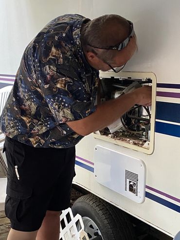 Mark repairing a refrigerator on a camper at a campground.