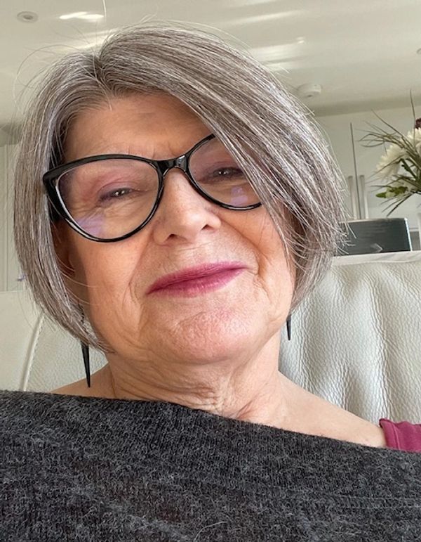 Smiling older woman with gray hair and glasses indoors.