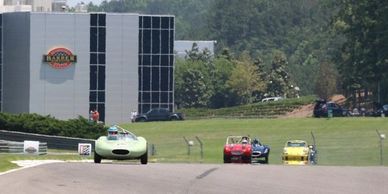 Four vintage race cars competing on a race track under a clear sky.