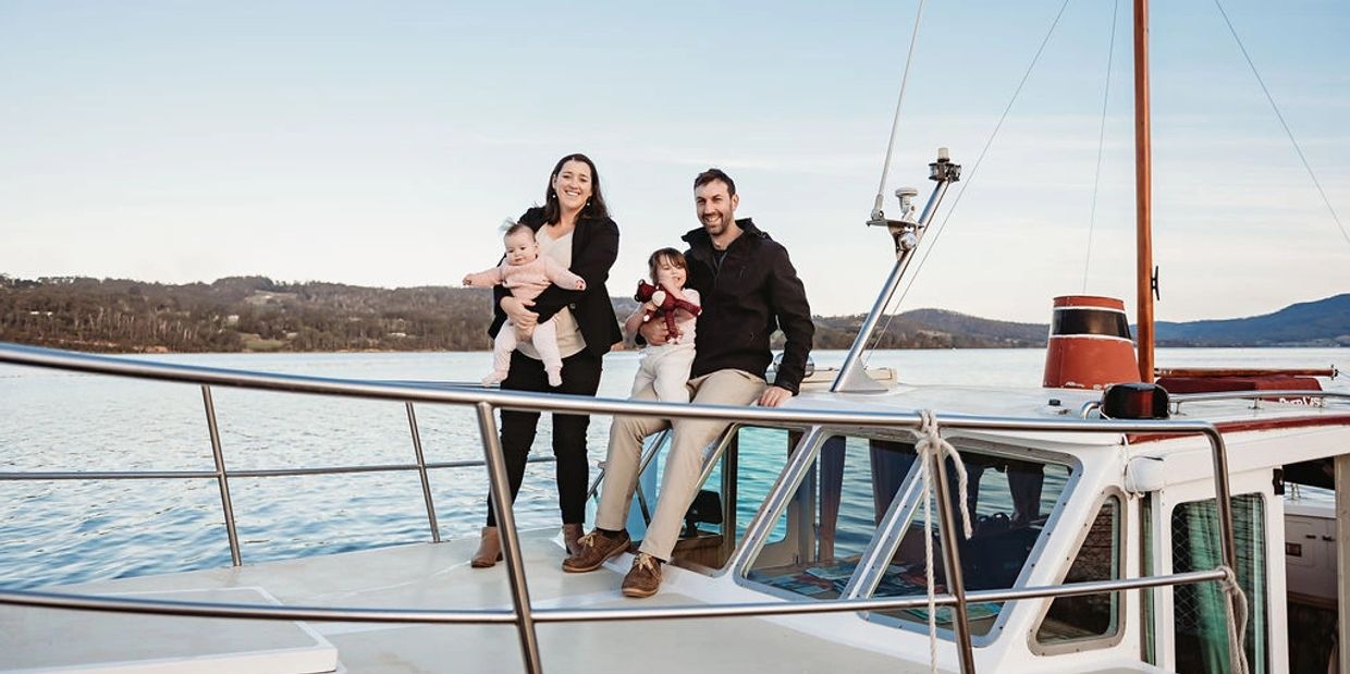 About Us - Huon River Cruises - The family behind the business on the bow of the luxury wooden boat