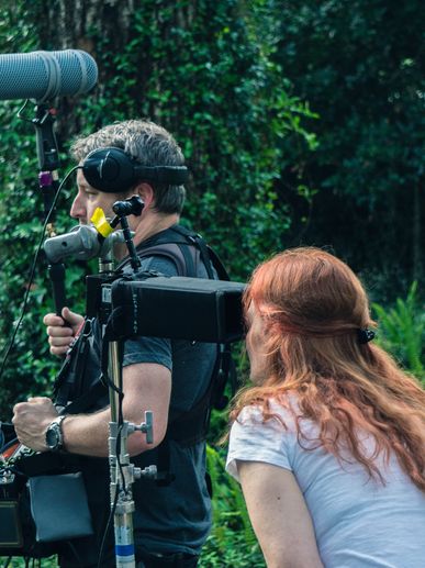 Two people working with filming equipment outdoors in a forest.