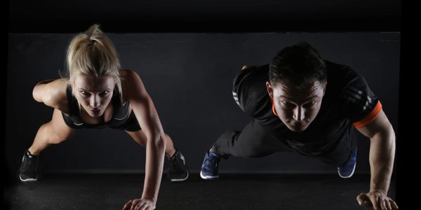 A man and woman doing push-ups side by side in a dark setting.