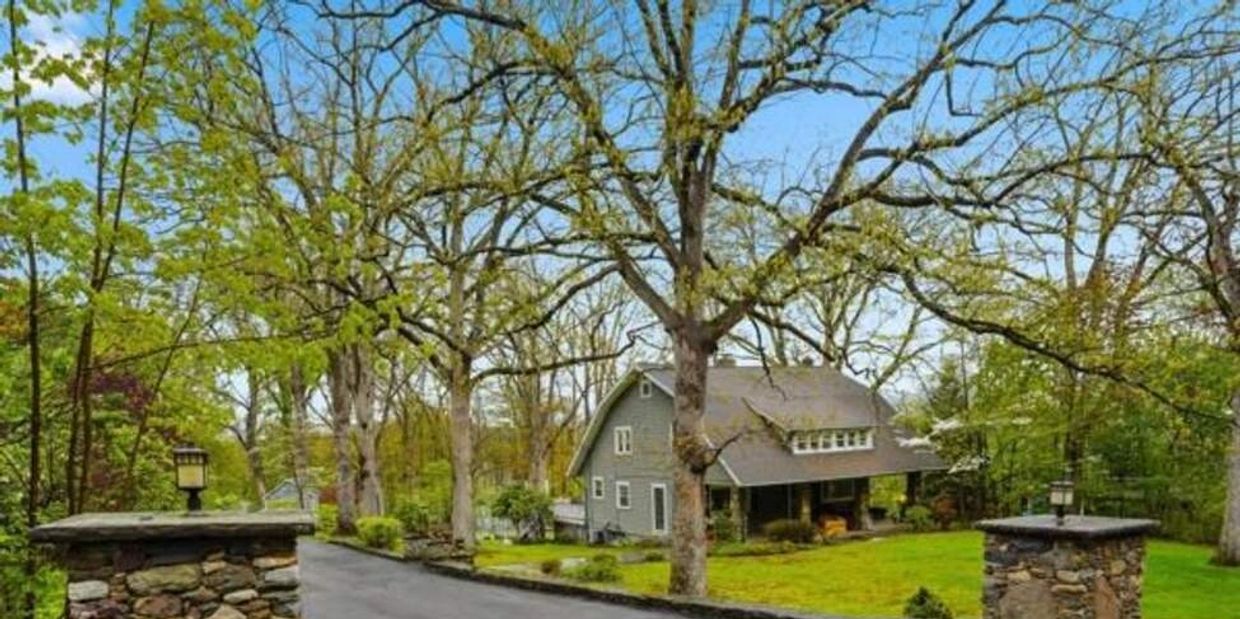 A cozy house surrounded by trees and a stone driveway entrance.