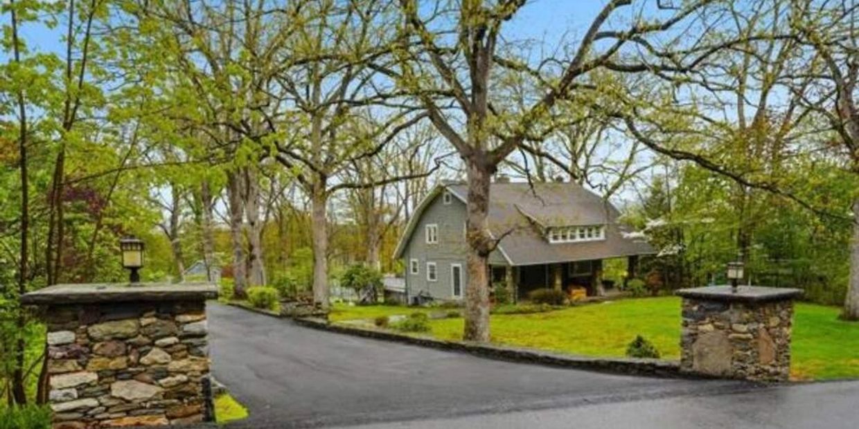 A house surrounded by trees and greenery with a paved driveway.