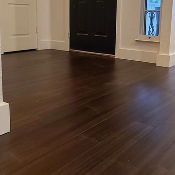 Dark wood flooring with white baseboards near a black front door and window.