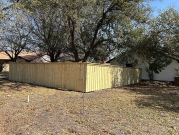 New wooden fence enclosing a backyard with trees and houses in the background.