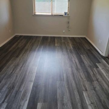 Empty room with dark wood flooring and a window with blinds.