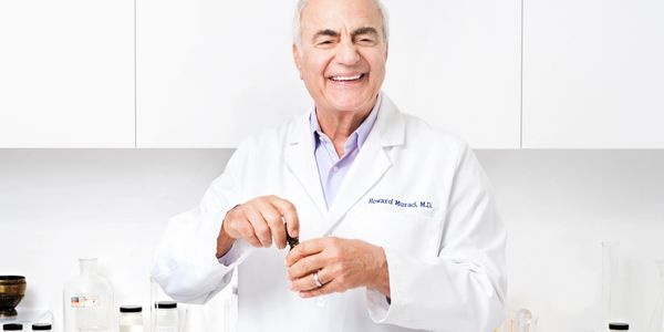 Smiling male scientist in lab coat holding a small bottle in a bright laboratory.