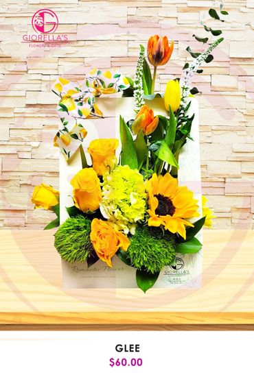 Bright yellow and orange floral arrangement with sunflowers and tulips in a white box.