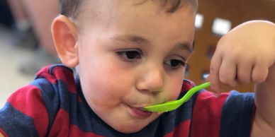 A young boy feeds himself with a small green spoon during feeding therapy