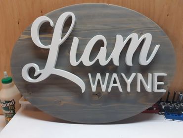 Wooden sign with the name Liam Wayne in white letters.