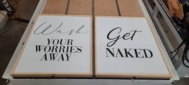 Two framed signs with playful bathroom messages about washing and getting naked.