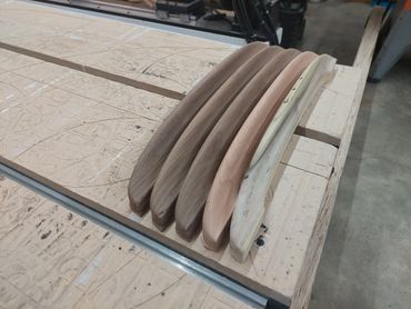 Five curved wooden pieces in varying wood tones on a workbench.