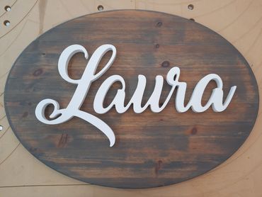 White cursive name 'Laura' on a dark wooden oval plaque.