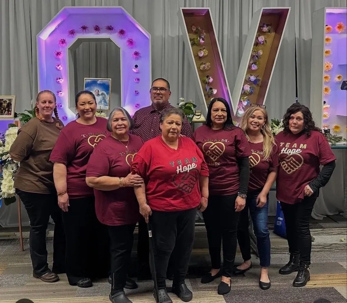 A group of people posing together wearing "Team Hope" shirts in front of illuminated letters.