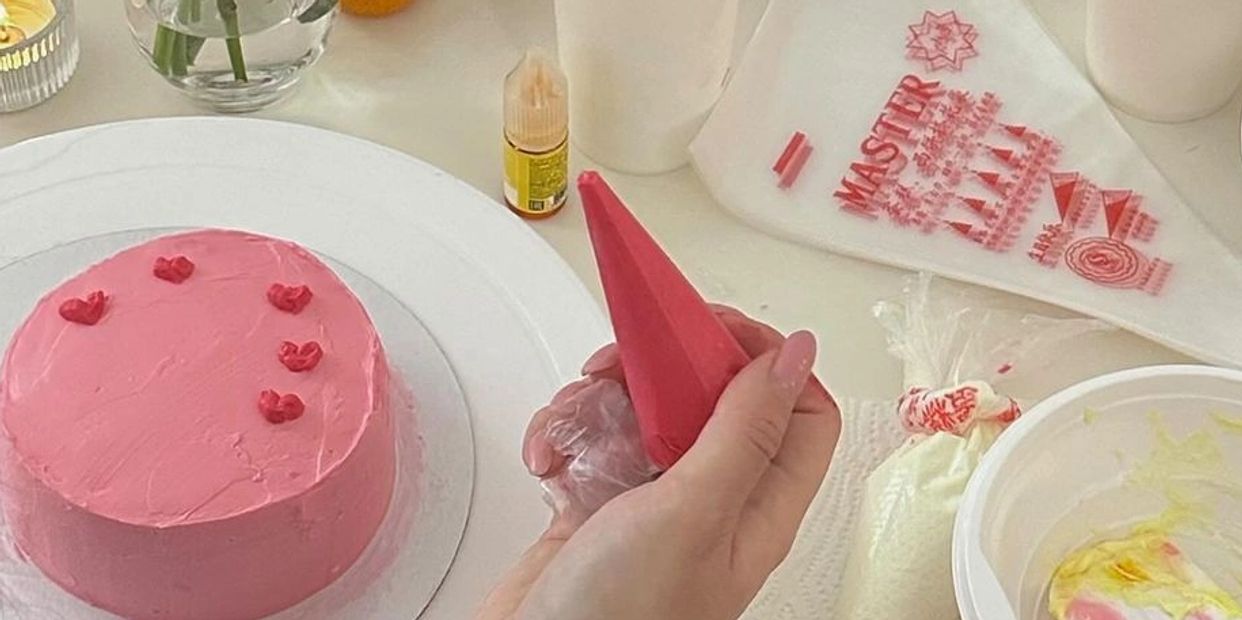 Person decorating a pink frosted cake with red icing hearts.
