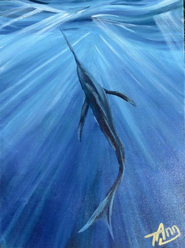 View of a billfish from behind, swimming through sun beams near the ocean's surface.