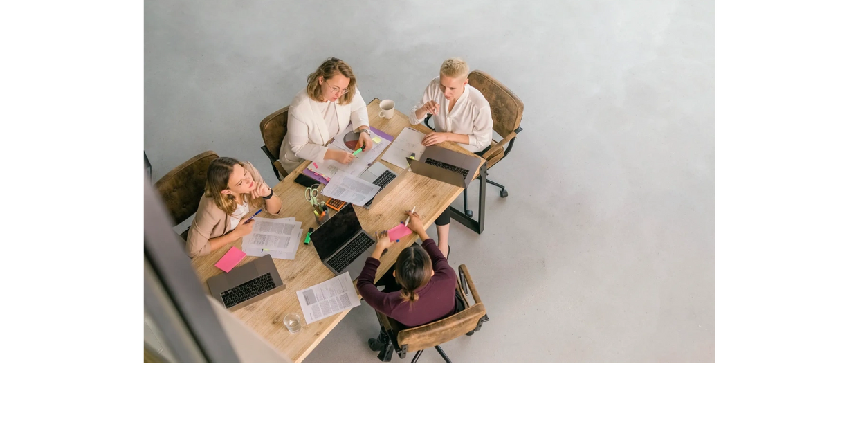 Four women collaborating around a table with laptops and documents.