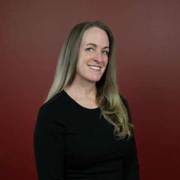 An older lady with blonde shoulder-length hair, wearing a black shirt. Smiles for her headshot.