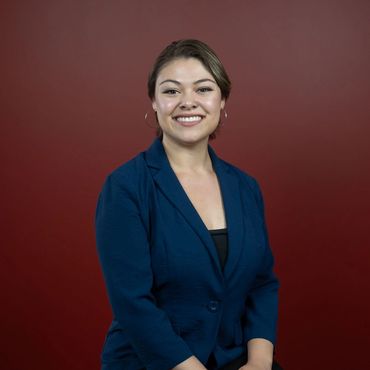 A young lady wearing a dark blue blazer, smiles at the camera for her headshot.