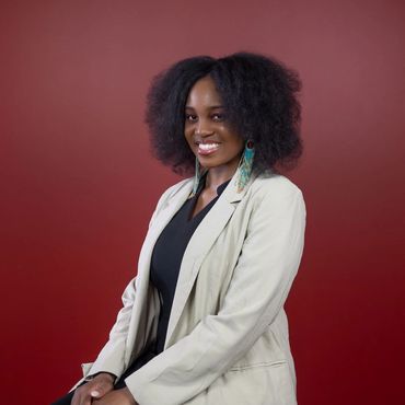 A headshot of a young African American lady with white blazer and tourquoise earrings.