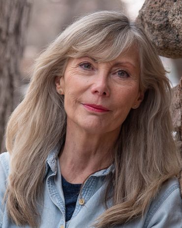 older woman leaning against a rock wall slightly smiling
