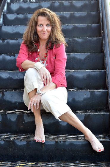 woman sitting on metal stairs, with her left leg turned in towards the right leg