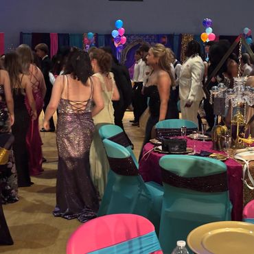 People dressed elegantly at a decorated event with colorful balloons and tables.