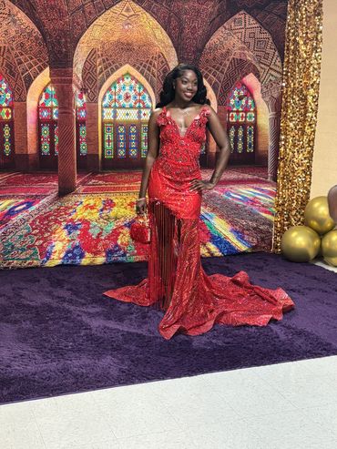 Woman in elegant red gown posing on purple carpet with ornate backdrop.