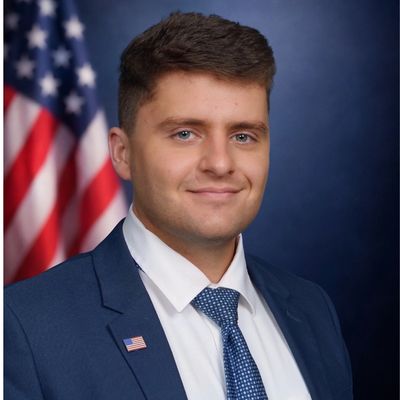 Young man in a suit with an American flag in the background.