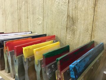Screen printing squeegees for printing tees, sitting on a shelf at our South Lyon production shop