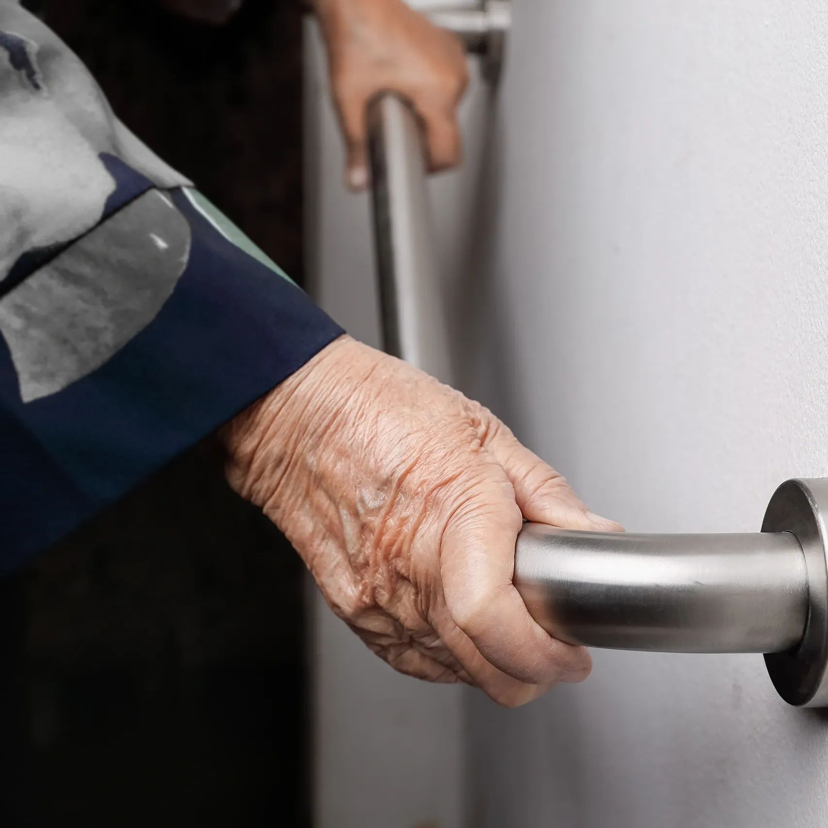 An elderly person holding a metal handrail.