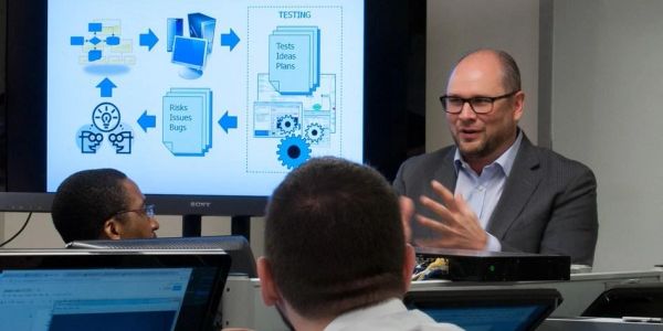 Man presenting to a group with flowchart on screen.