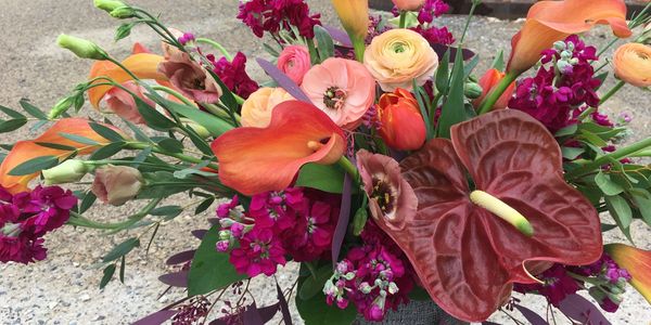 A vibrant bouquet with orange, pink, and deep red flowers in various shapes and sizes.