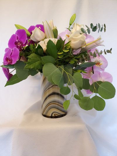 dark and light purple orchids with eucalyptus branches in and elegant brown and creamy vase.Oceana Florist deliver flowers in Vancouver. We are Vancouver house of flowers, Prince Rupert Florist & King Edward Florist.