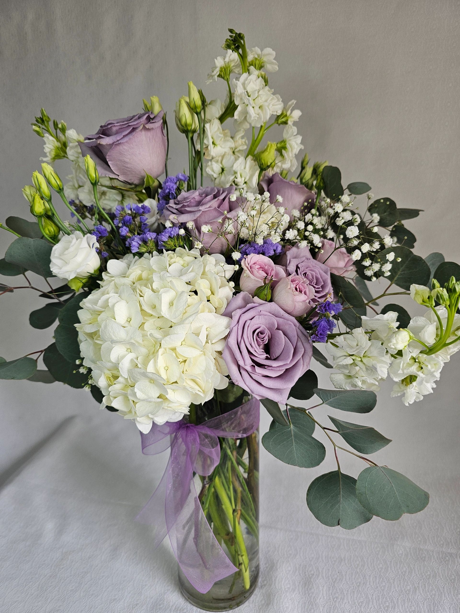 Elegant bouquet with purple roses and white flowers in a glass vase with a purple ribbon.