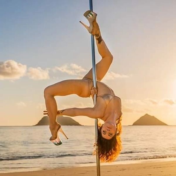A woman performing a pole dance move on the beach at sunset.
