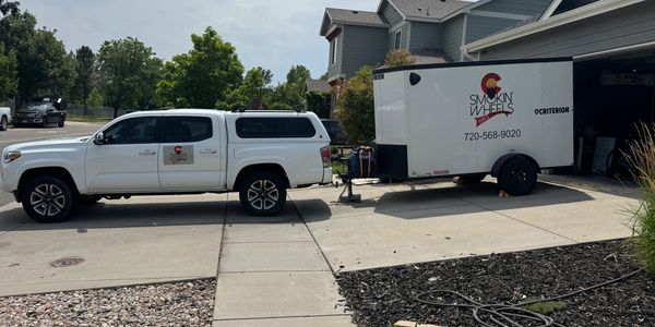 White truck towing a Smokin' Wheels BBQ trailer in a residential driveway.