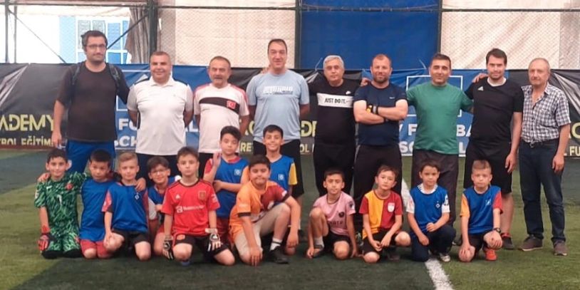 Futbol sahasında çocuklar ve yetişkinler topluca poz veriyor.
