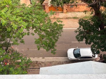 White car parked beside a quiet street with trees overhead.