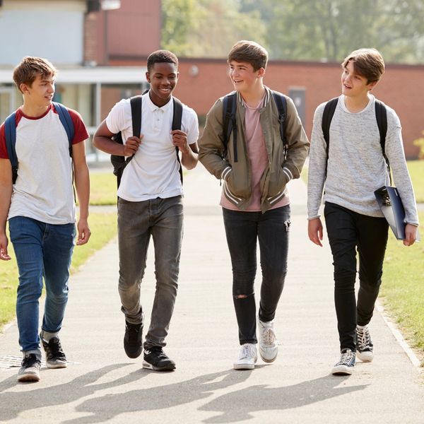 Four teenaged boys walking away from a school with backpacks on.