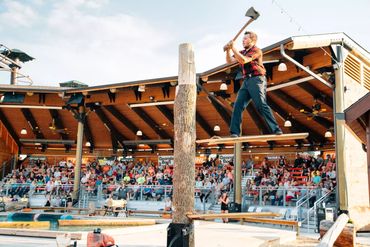 Man performing a lumberjack axe chop on a high wooden platform.