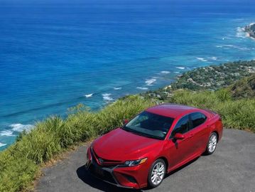 Red Toyota car parked by a coastal cliff with ocean view.