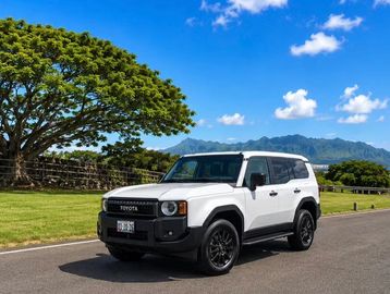 White Toyota SUV on a scenic road with mountains and blue sky.