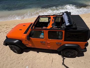 Orange Jeep Wrangler on a sandy beach by the ocean.