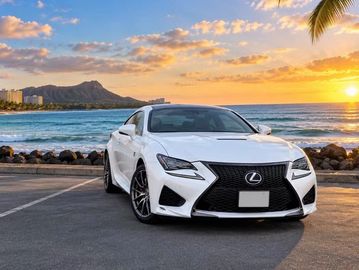 White Lexus car parked near beach at sunset.