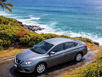 Silver sedan parked near a coastal road with ocean waves.