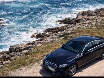 Black Mercedes parked near rocky coastline with waves.
