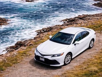 White car parked on a rocky coastal path.