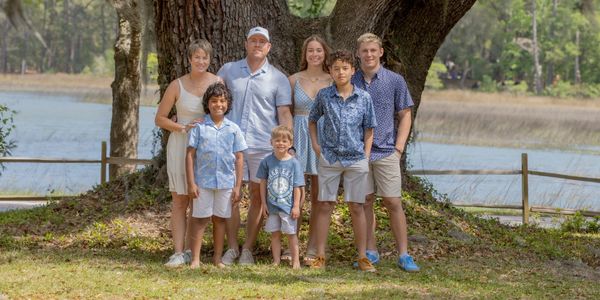 Family posing outdoors near a large tree by a lake.
